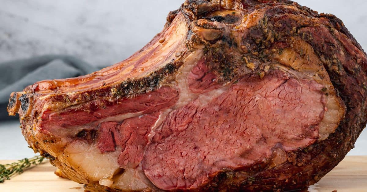 A close-up of a cooked prime rib roast resting on a wooden cutting board.