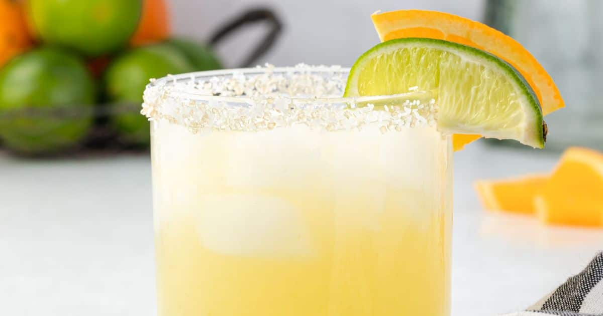 A margarita in a glass with a salted rim, garnished with lime and orange slices.