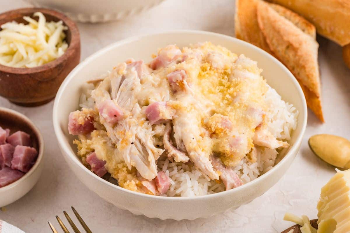Bowl of creamy shredded chicken and ham over white rice, with bread and cheese on the side.