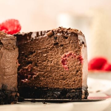 A close-up of a sliced chocolate cheesecake with raspberries and a dark cookie crust.