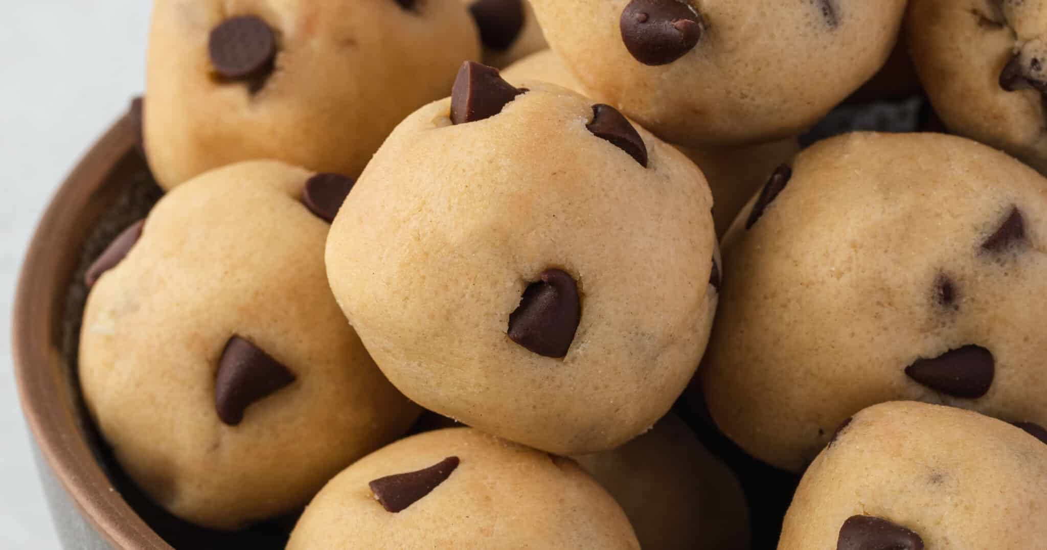 A close-up of round chocolate chip cookie dough balls in a brown bowl.