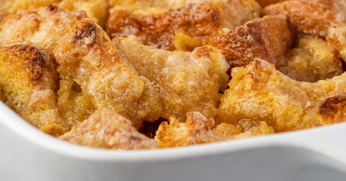 Close-up of golden-brown bread pudding in a white baking dish.