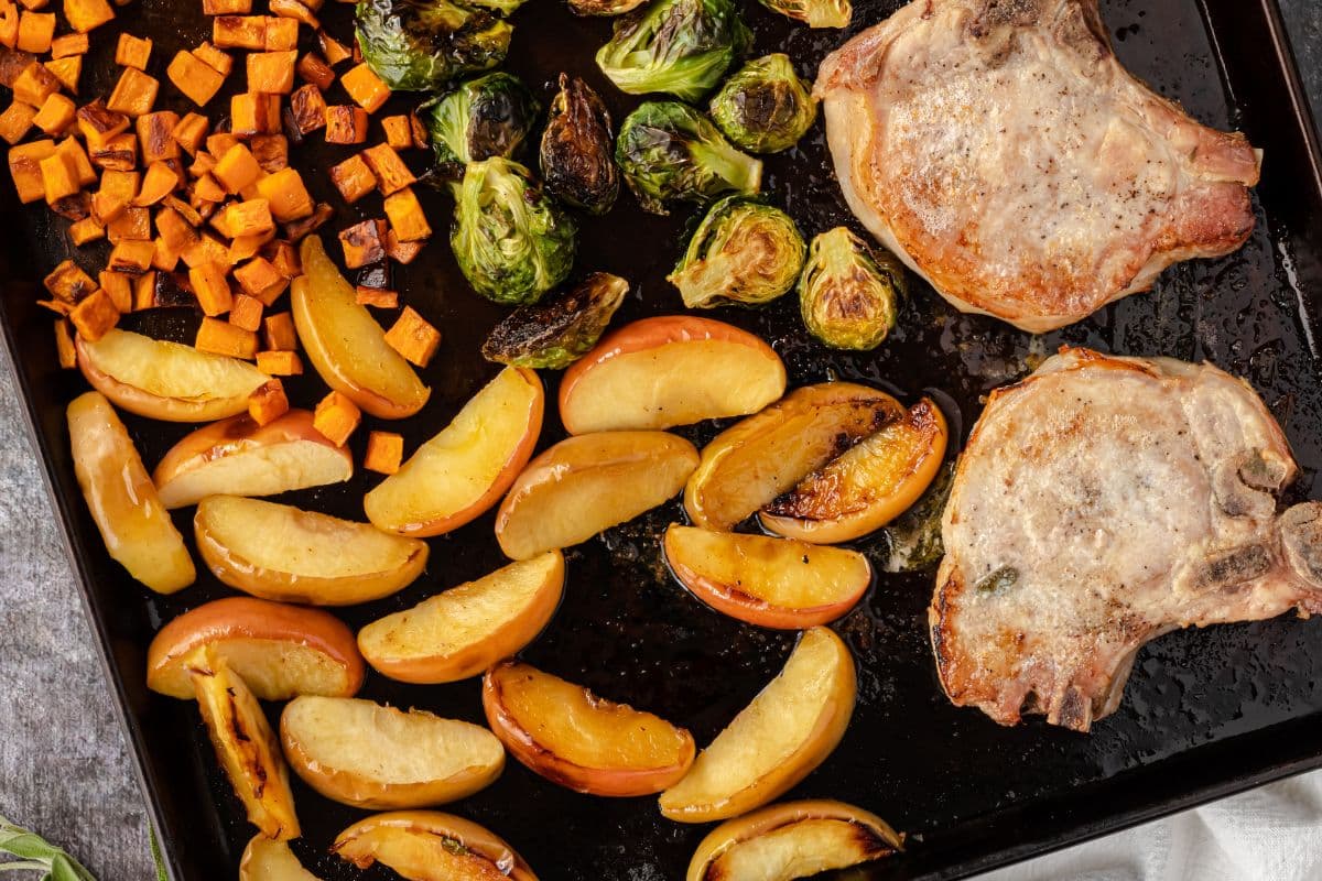 Sheet pan with roasted pork chops, apple slices, Brussels sprouts, and diced sweet potatoes.