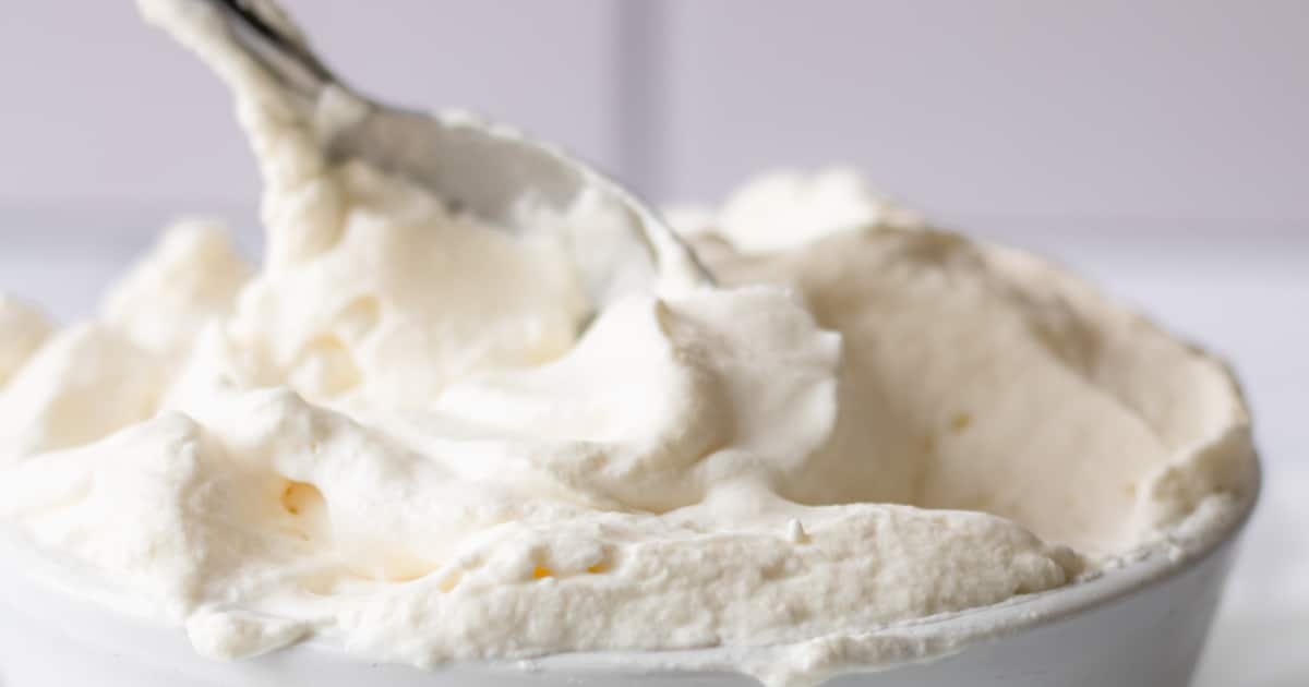 A bowl of whipped cream with a spoon scooping some out.
