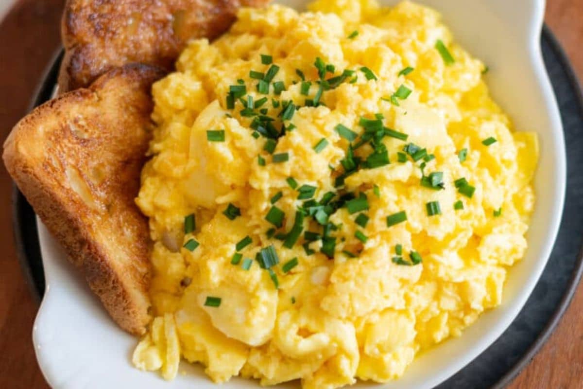 A plate of scrambled eggs topped with chopped chives, served with two slices of toasted bread.