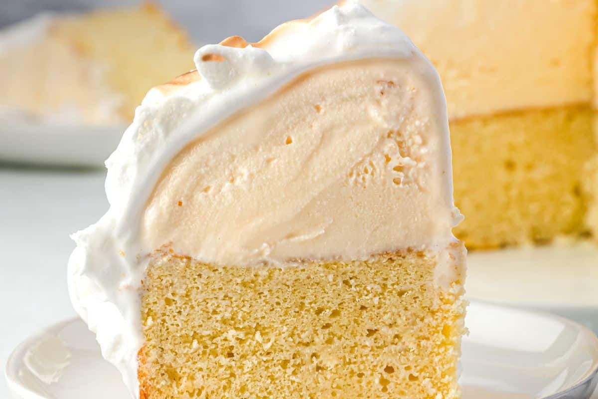 A slice of vanilla cake topped with a thick layer of creamy frosting on a white plate.