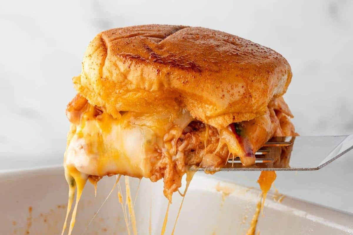A cheesy, golden-brown sandwich with melted cheese and pulled meat on a spatula.