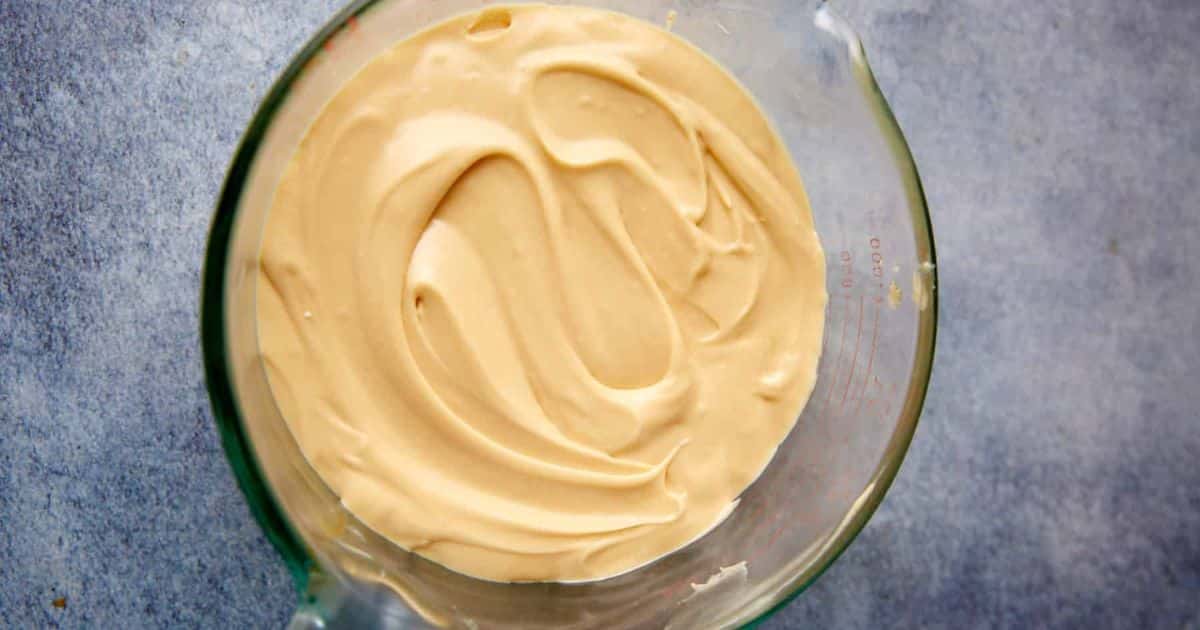 A glass bowl filled with smooth, creamy batter on a textured gray surface.