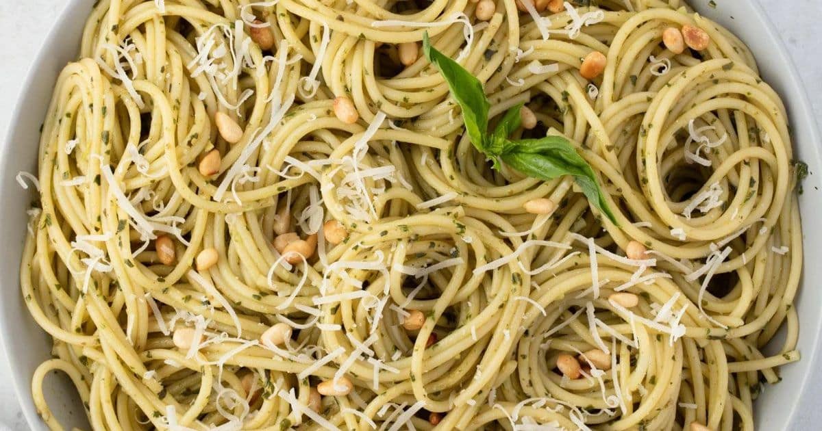 Spaghetti with pesto sauce, grated cheese, pine nuts, and a sprig of basil on top.