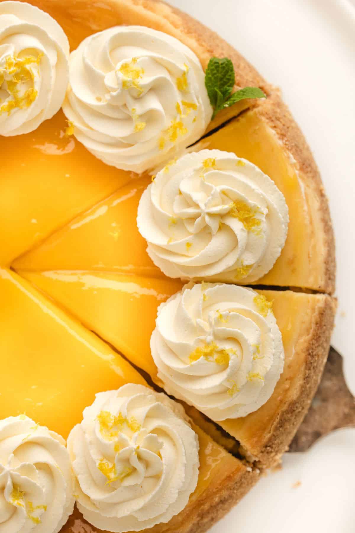 A lemon pie topped with whipped cream and lemon zest, sliced and served on a white plate.