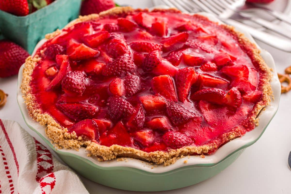 A strawberry pie with a crumbly crust, filled with glazed strawberries, in a green pie dish.