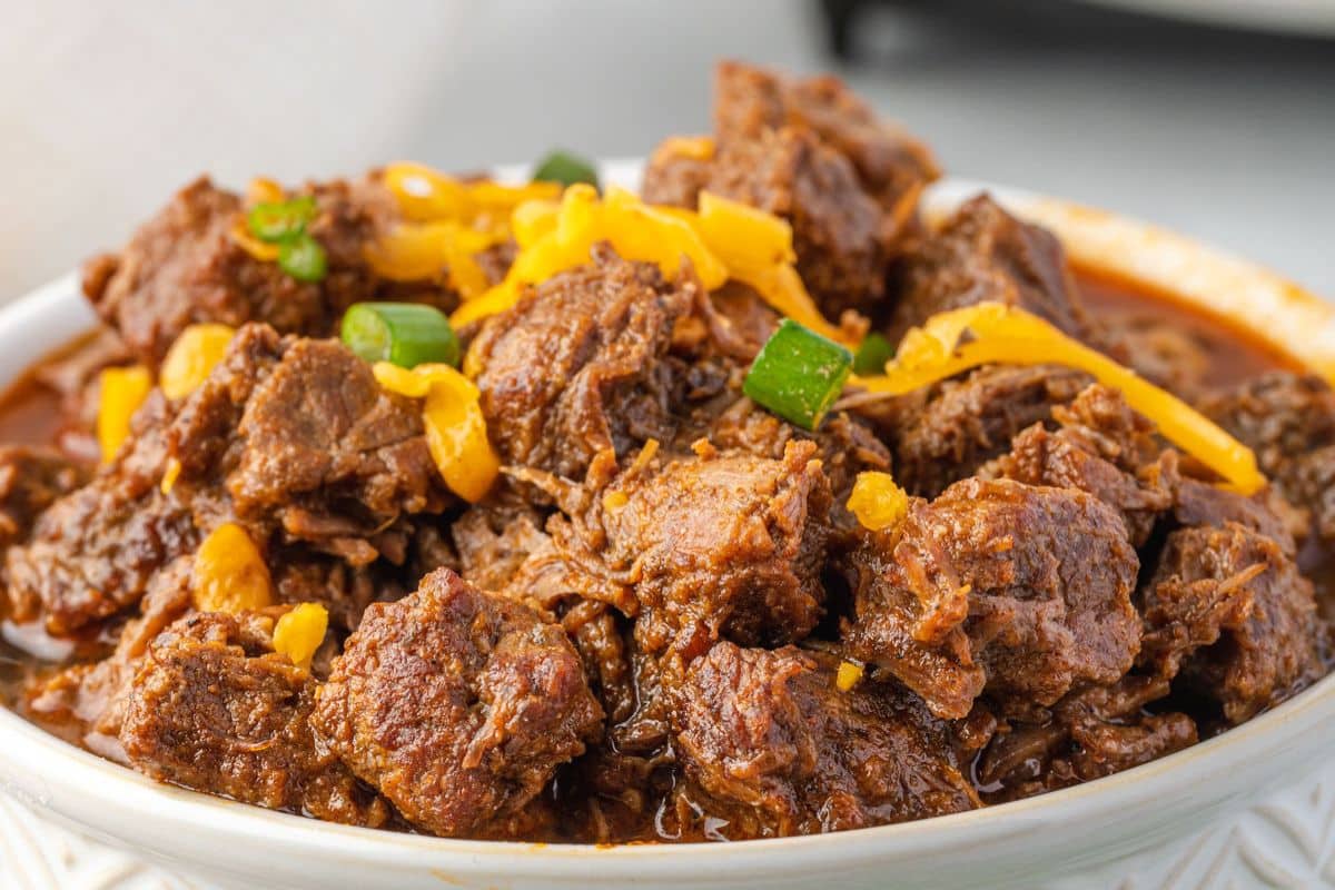 A bowl of chunky beef chili topped with shredded cheese and sliced green onions.