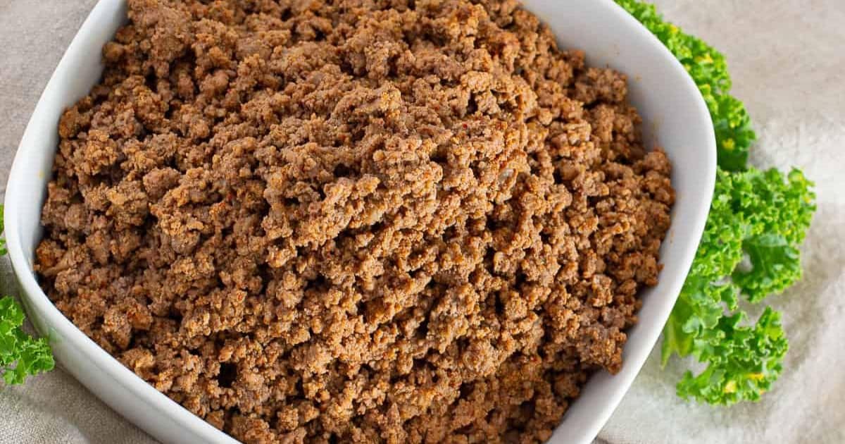 Cooked ground beef in a white bowl, garnished with fresh parsley on the side.