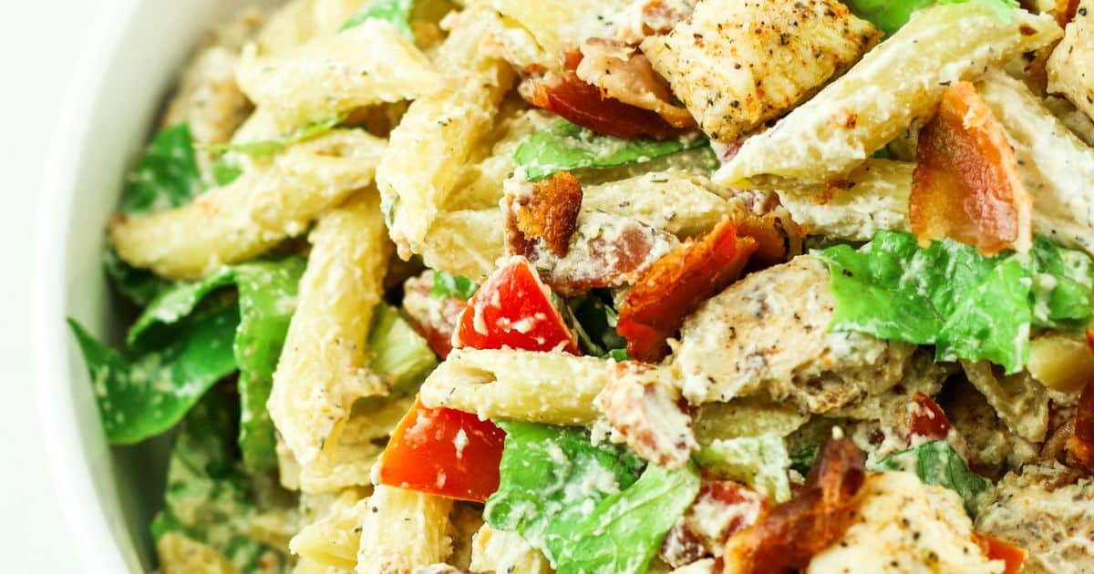 Close-up of a creamy pasta salad with penne, grilled chicken, lettuce, bacon, and diced tomatoes.