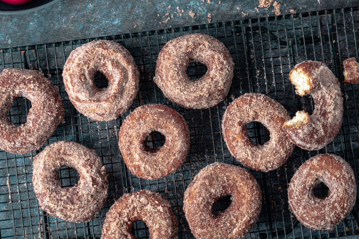 Cinnamon sugar donuts on a cooling rack, with one donut partially eaten.