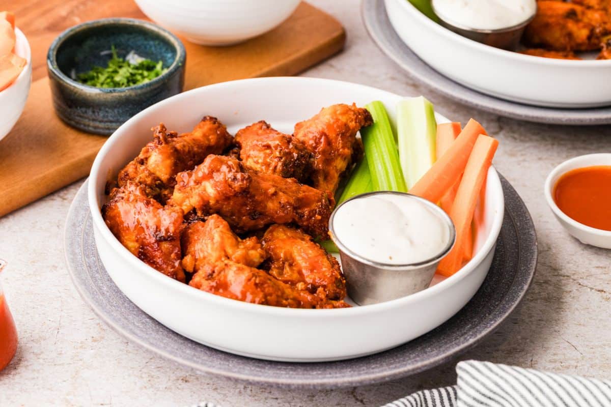A bowl of buffalo wings with celery, carrot sticks, and ranch dip on a plate.