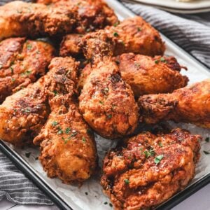 A tray of crispy fried chicken drumsticks and thighs garnished with chopped herbs.