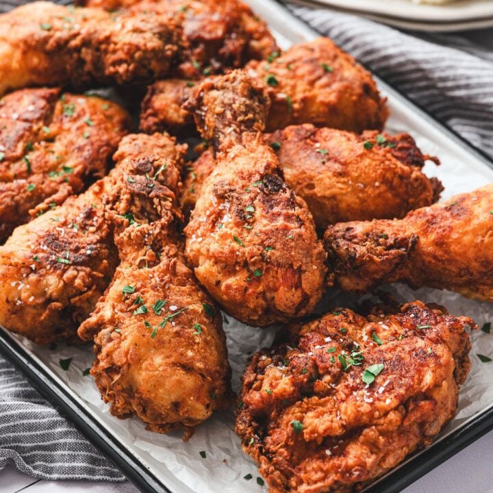 A tray of crispy fried chicken drumsticks and thighs garnished with chopped herbs.
