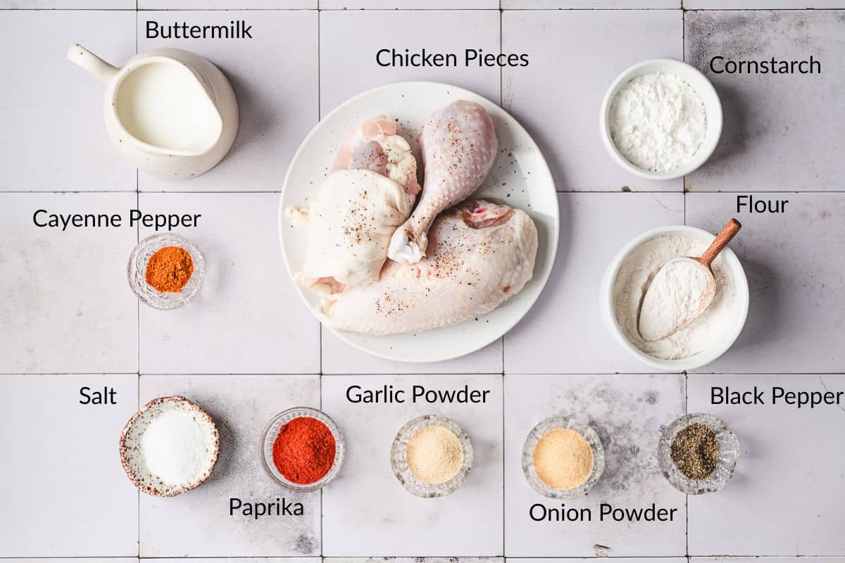 A flat lay of labeled fried chicken ingredients including chicken, spices, flour, cornstarch, and buttermilk.