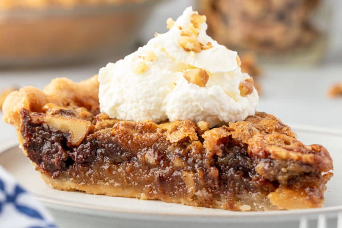 A slice of pecan pie topped with whipped cream and chopped nuts on a plate.