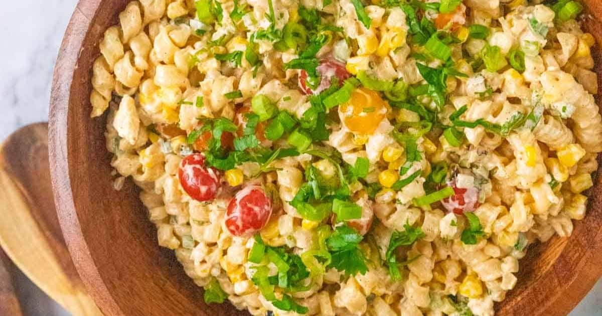 A wooden bowl filled with creamy pasta salad, topped with chopped green onions and herbs.