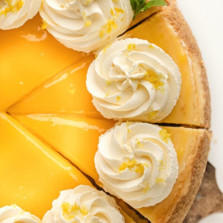 A lemon pie with whipped cream swirls and lemon zest, sliced and ready to serve.