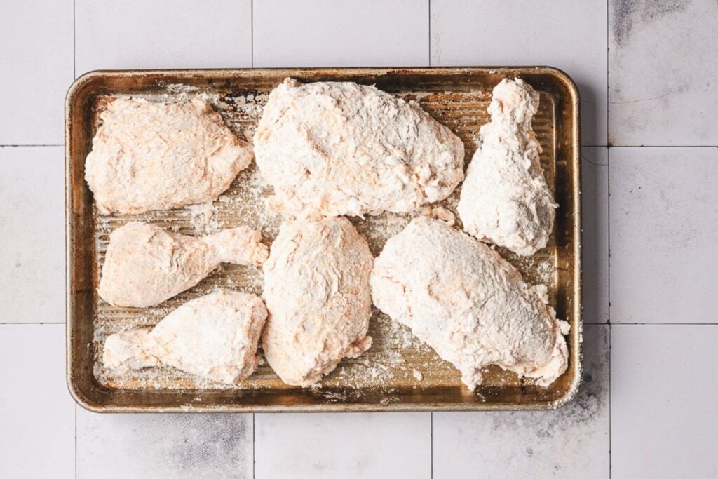Raw chicken pieces coated in flour arranged on a baking sheet, ready for cooking.