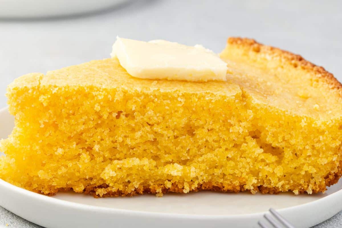 A slice of cornbread with a pat of butter on top, served on a white plate.