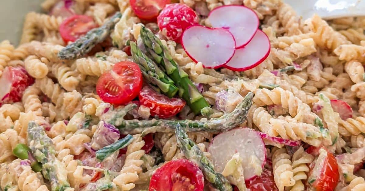 Rotini pasta salad with asparagus, cherry tomatoes, radish slices, and a creamy dressing.