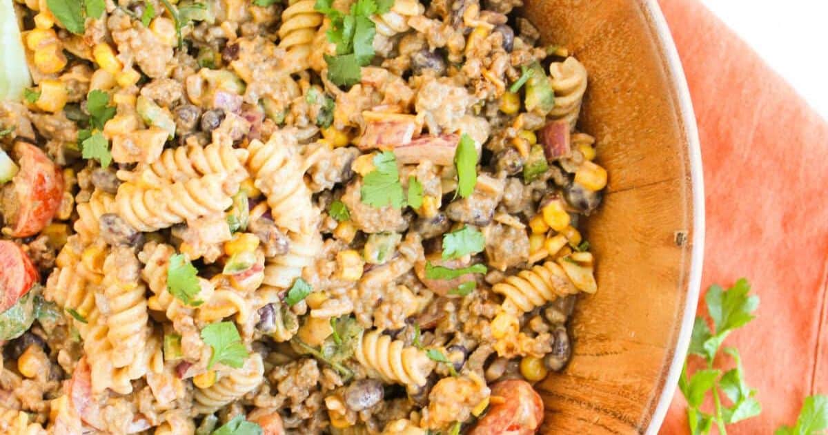 A bowl of creamy pasta salad with rotini, ground meat, beans, corn, tomatoes, and fresh cilantro on top.