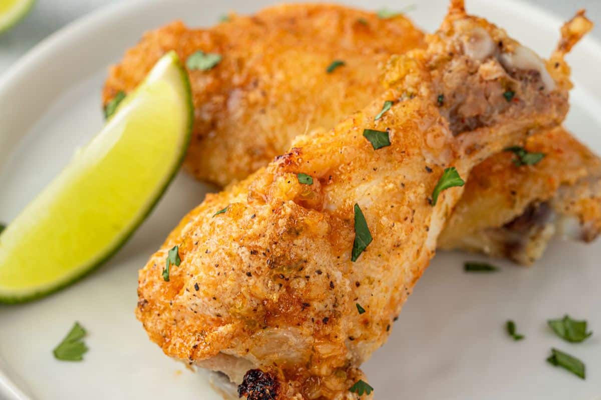 Crispy baked chicken drumstick garnished with herbs, served with a lime wedge on a white plate.