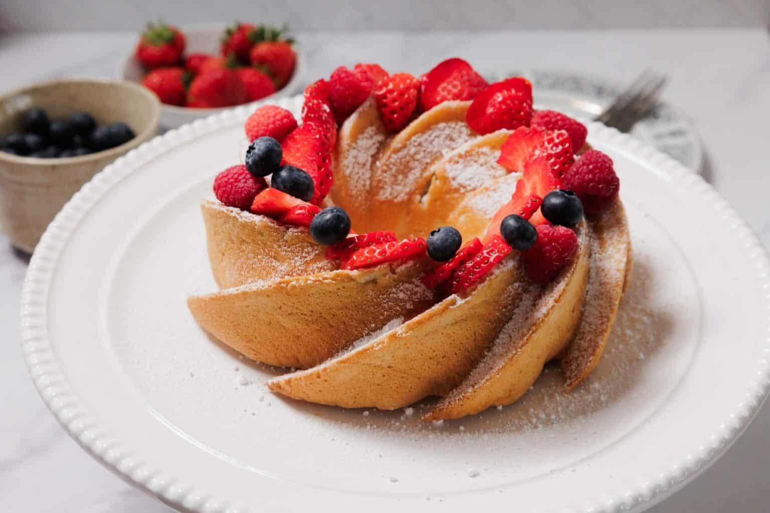 A Bundt cake topped with strawberries, raspberries, blueberries, and a dusting of powdered sugar.
