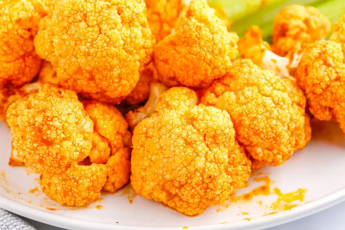 Close-up of crispy buffalo cauliflower bites on a white plate, coated in orange sauce.