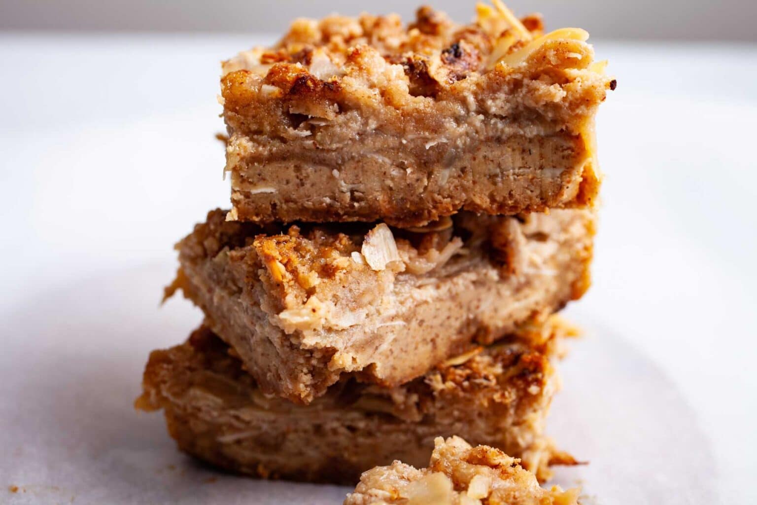 Three stacked baked oatmeal bars with a golden, crumbly texture on a white surface.