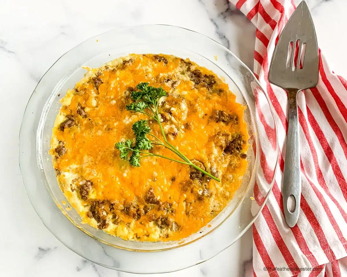 A baked casserole with melted cheese and parsley on top, beside a spatula and a red striped napkin.