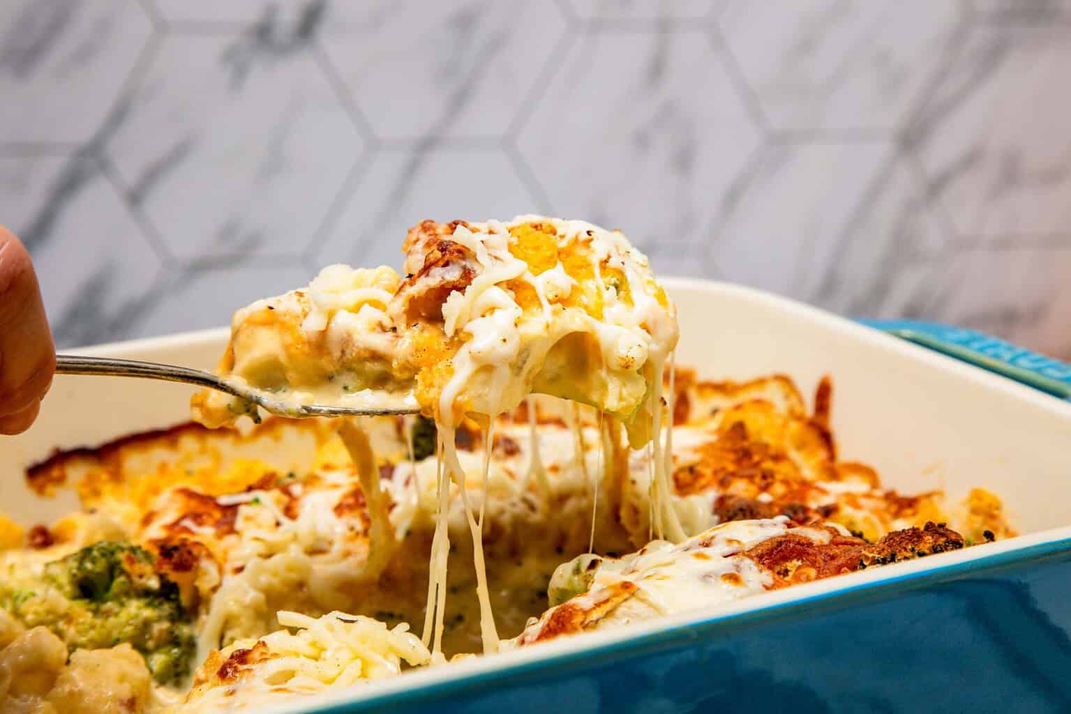 A spoon lifts cheesy, baked casserole from a blue dish, with melted cheese stretching.