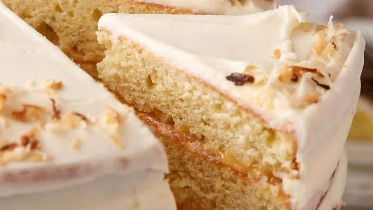 A close-up of a sliced coconut cake with white frosting and toasted coconut flakes on top.