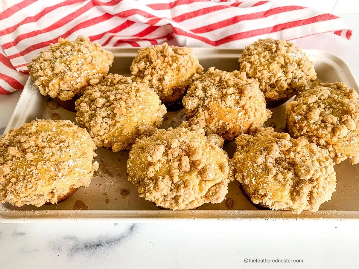 A tray of nine crumb-topped muffins sits on a white surface next to a red and white striped cloth.