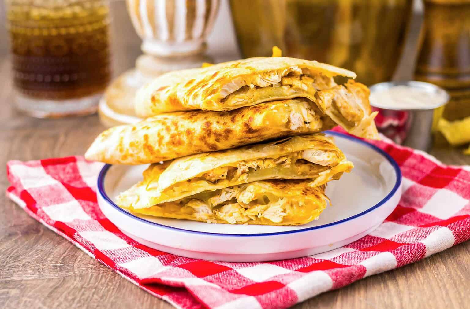 Three pieces of stuffed flatbread with chicken filling stacked on a plate, on a red checkered cloth.