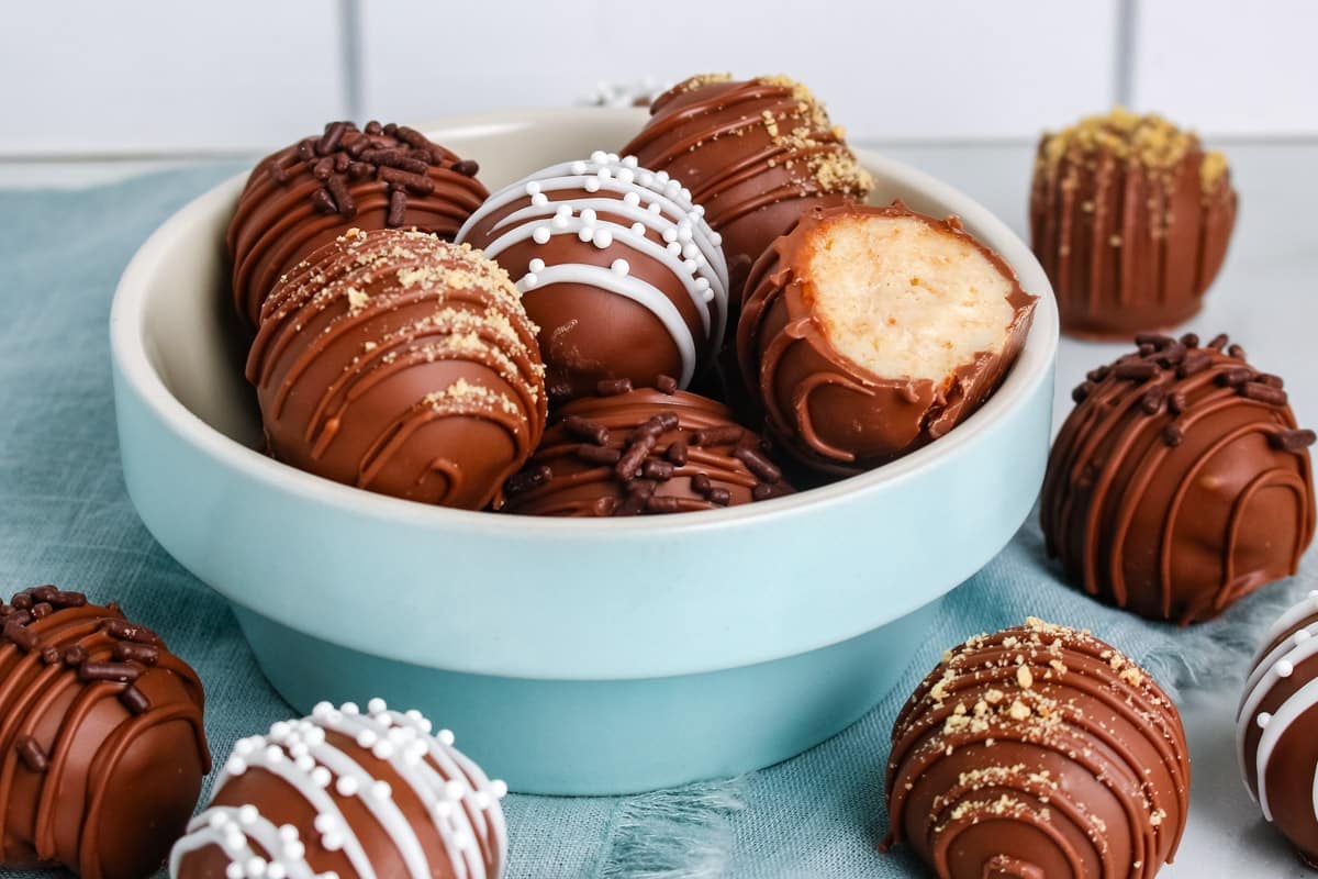 A bowl of assorted chocolate truffles, some topped with sprinkles, with one truffle bitten to show the filling.