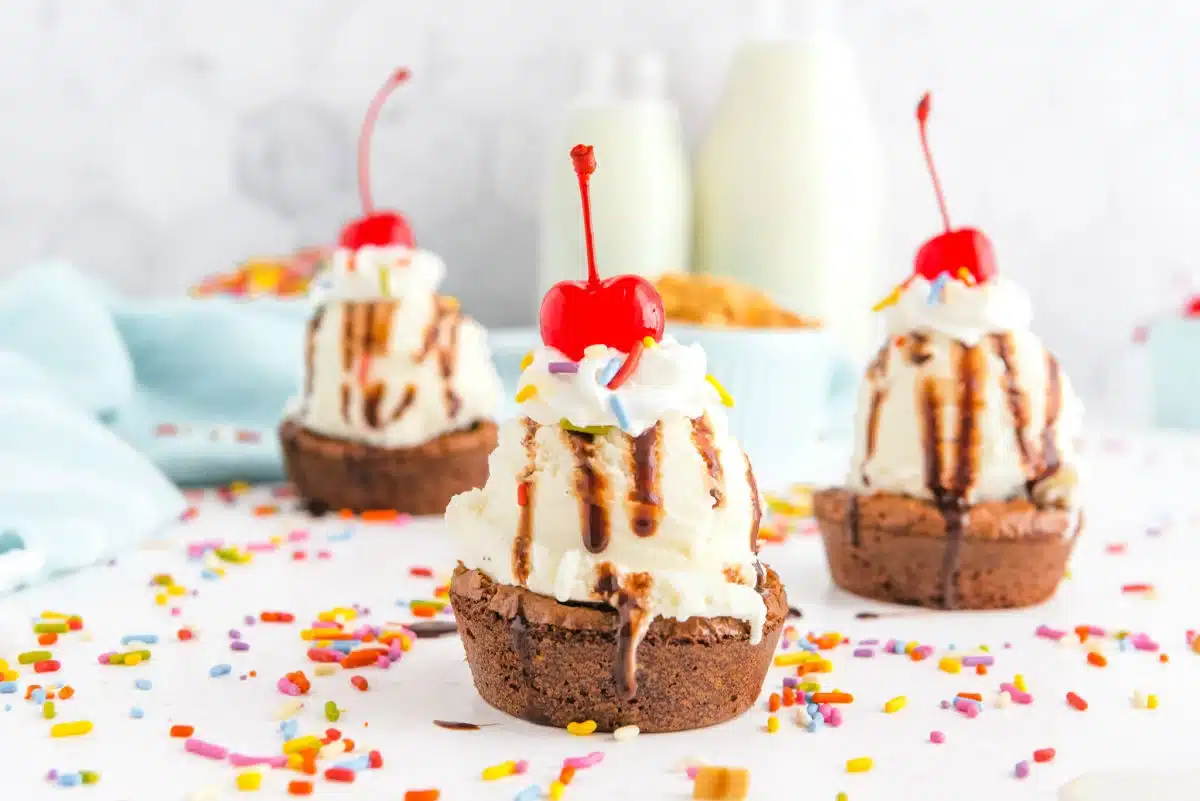 Three brownie sundaes with vanilla ice cream, whipped cream, cherries, chocolate syrup, and sprinkles.