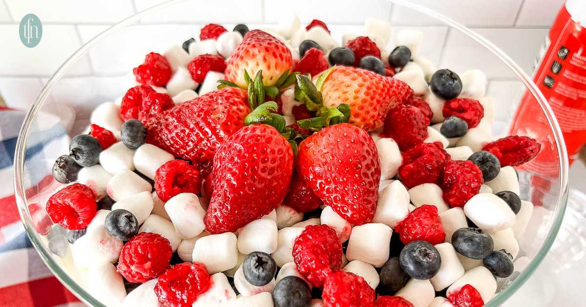 A glass bowl filled with strawberries, raspberries, blueberries, and mini marshmallows.