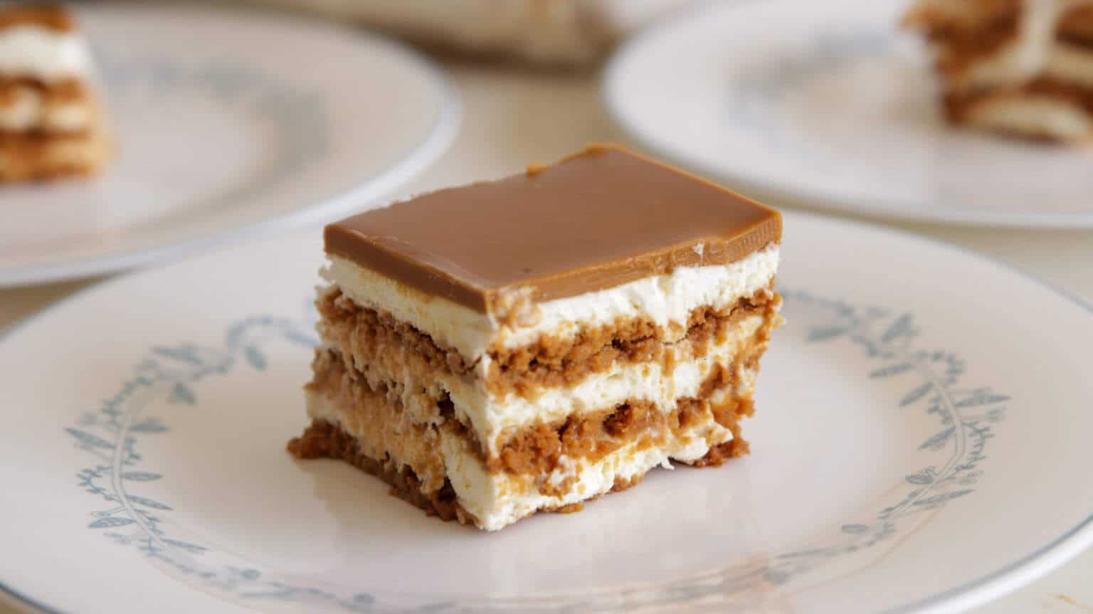 A slice of layered cake with caramel topping and cream filling on a white plate with a blue floral design.