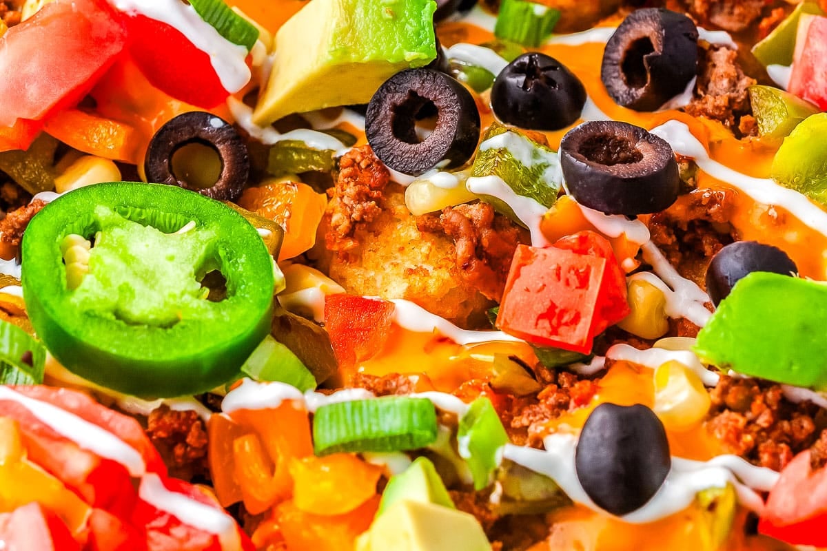 Close-up of loaded nachos topped with ground beef, cheese, olives, jalapeños, avocado, tomato, and sour cream.