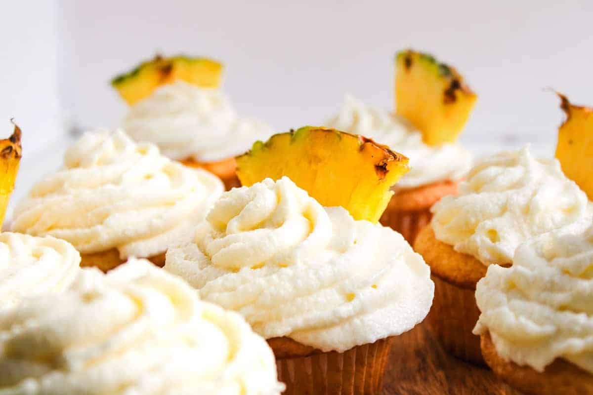 Cupcakes with swirled white frosting, each topped with a slice of fresh pineapple.