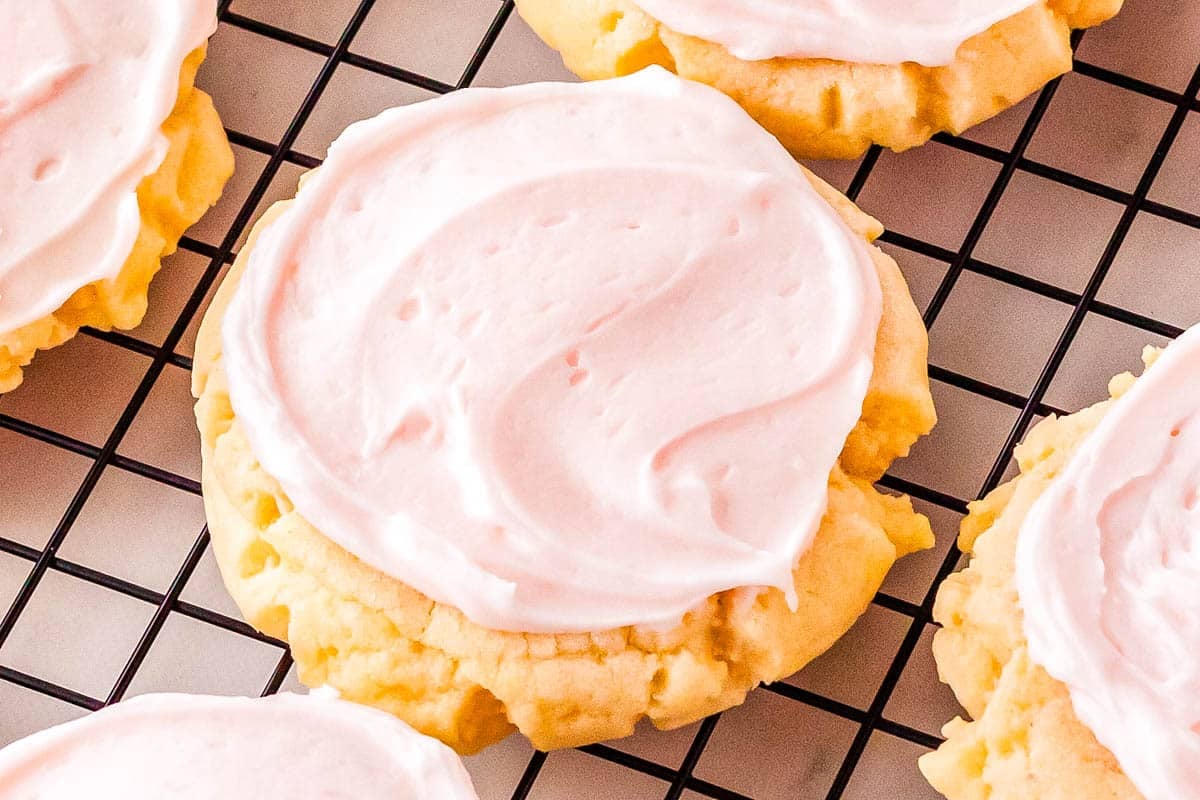 A sugar cookie with pink frosting on a black wire cooling rack.