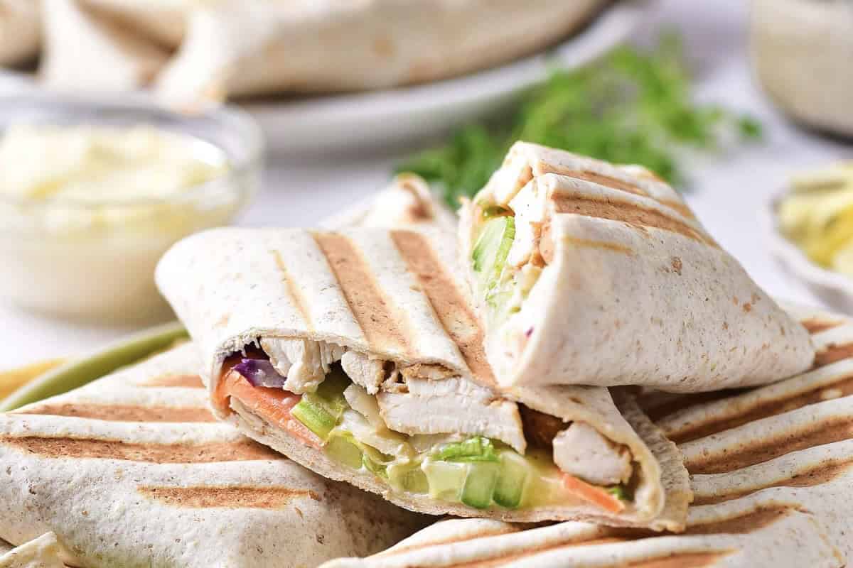 Grilled chicken wraps filled with lettuce, cucumber, and vegetables, stacked on a plate.