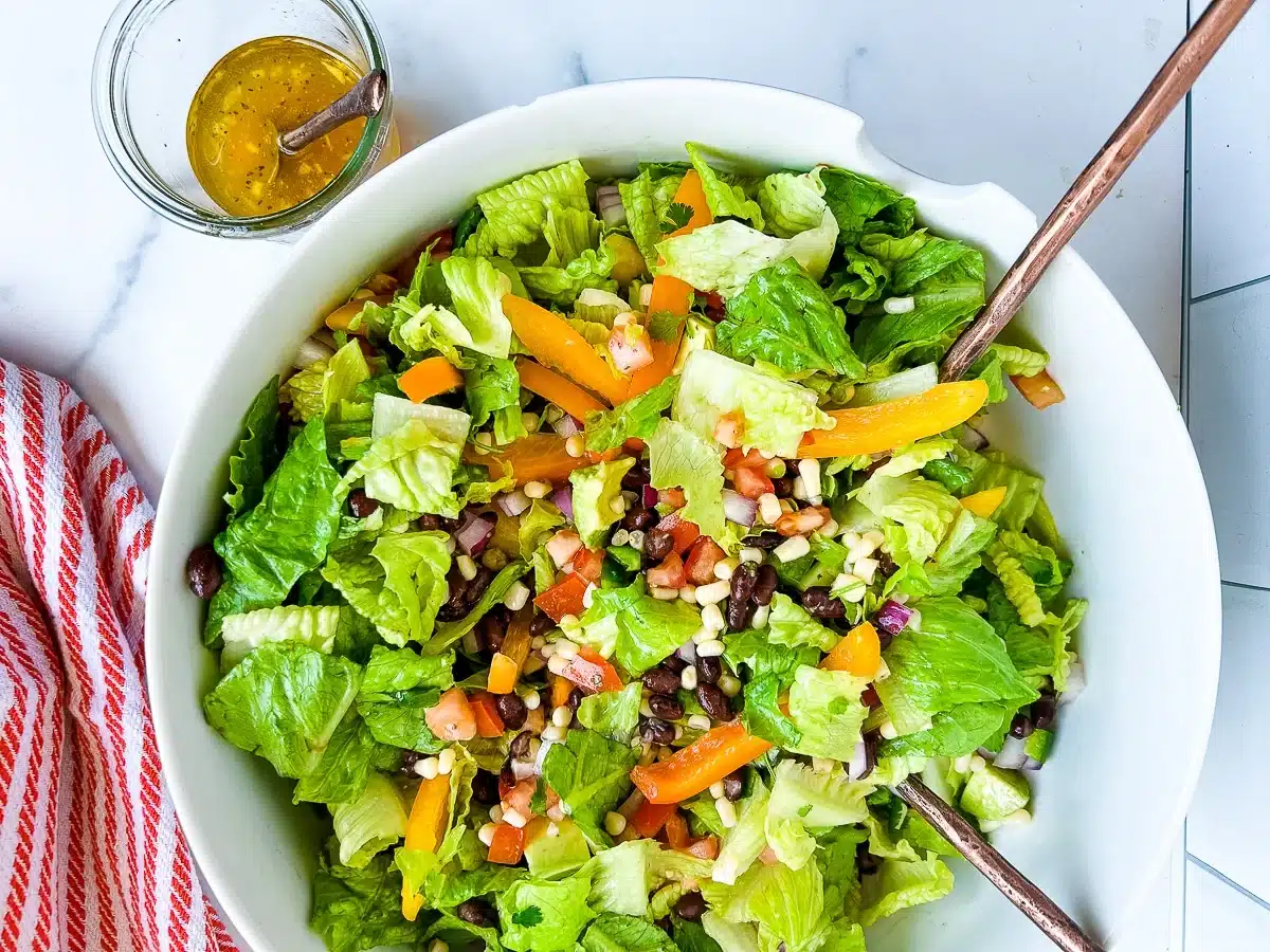 A bowl of colorful salad with lettuce, black beans, corn, peppers, and dressing on the side.