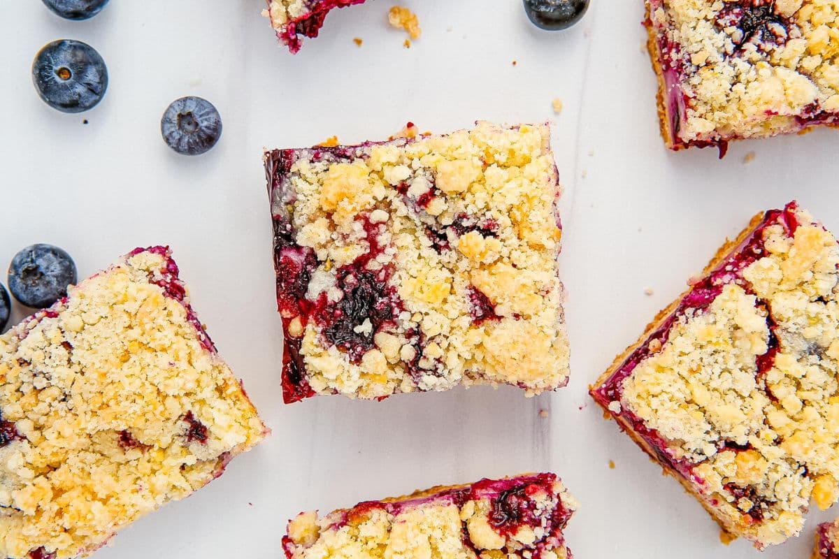 Close-up of blueberry crumble bars and fresh blueberries on a white surface.