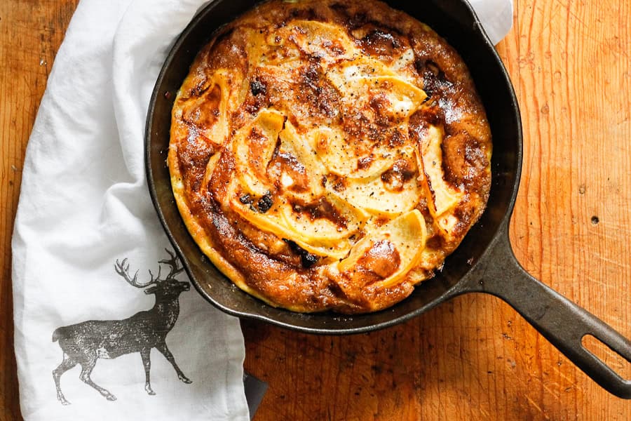 A baked apple dessert in a cast iron skillet, resting on a wooden surface with a deer-printed white cloth.